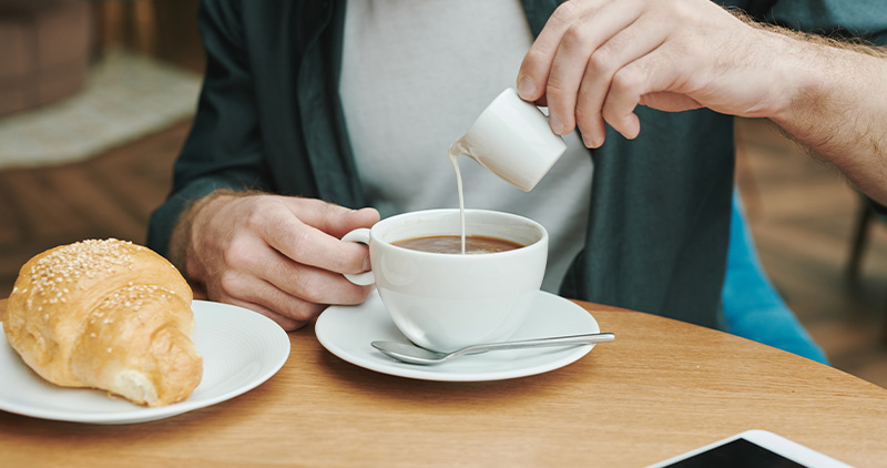 Homme versant du lait dans son café dans un restaurant. 