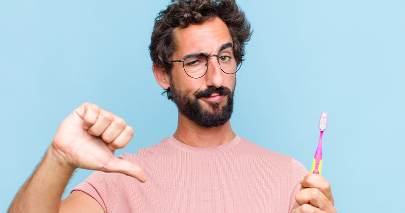 Monsieur avec une brosse à dent pour enfant dans sa main gauche et faisant un pouce vers le bas avec sa main droite.